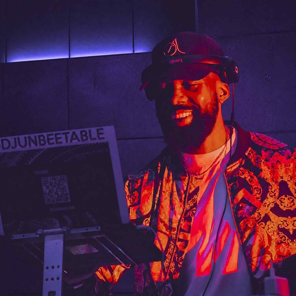 DJ Unbeetable smiling at the booth in an ornate jacket with headphones