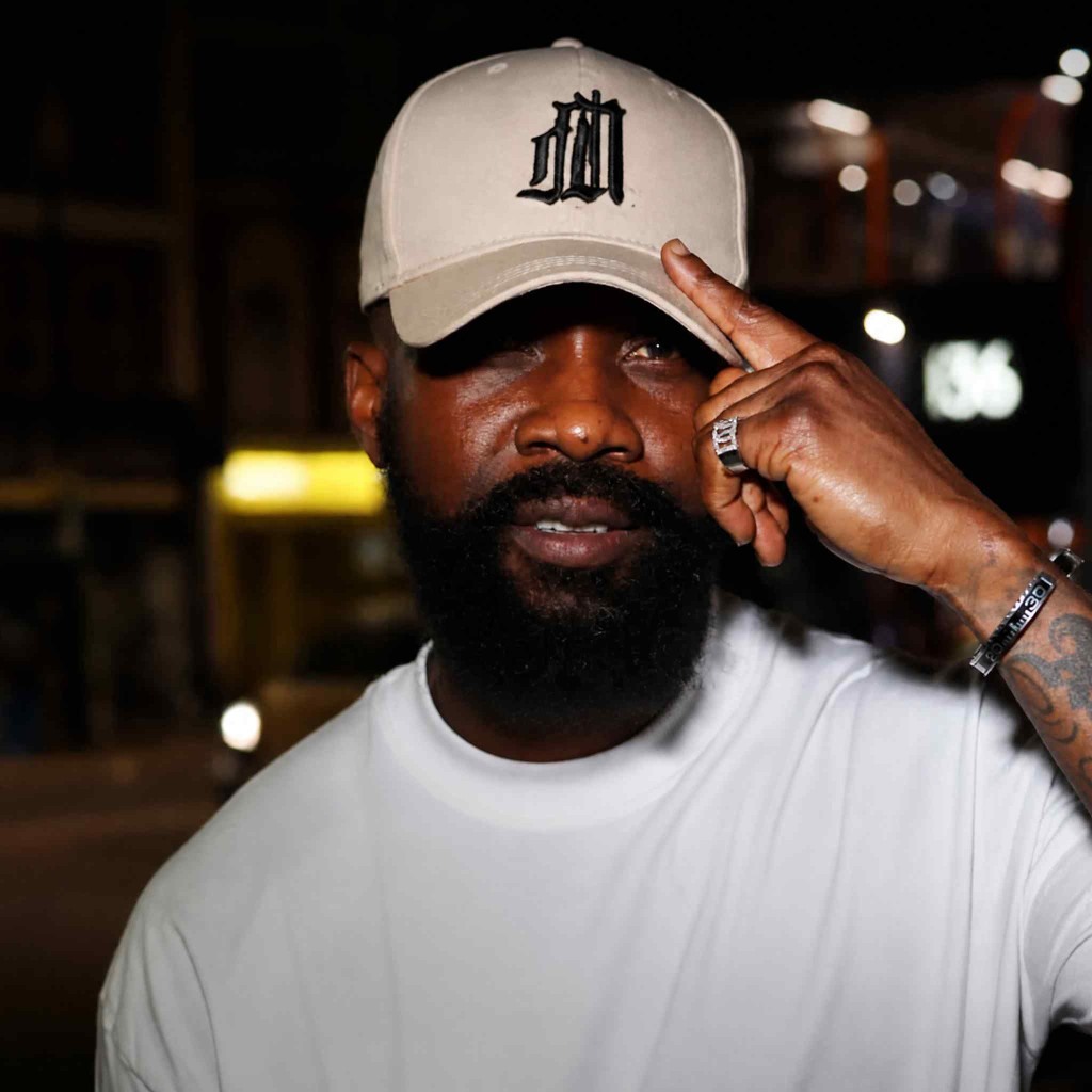 DJ Unbeetable in a tan cap and white tee against city lights